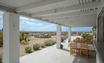a patio with a wooden table and chairs , surrounded by desert landscape under a covered walkway at Natura Villas in Naxos