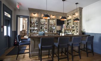 a well - lit bar area with a long wooden counter , multiple chairs , and various bottles and glasses on display at The Little Inn of Bayfield