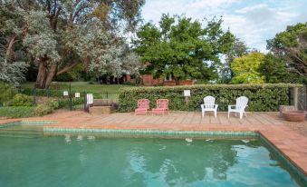 a pool with a brick deck and white chairs is surrounded by trees and bushes at Stay in Mudgee