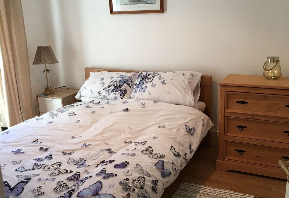 a cozy bedroom with a bed , nightstand , dresser , and lamp , decorated with butterflies on the bedding at Town Apartments