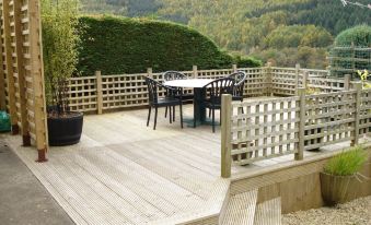 a wooden deck with a dining table and chairs set up for a meal , surrounded by trees and mountains at Wildwinds