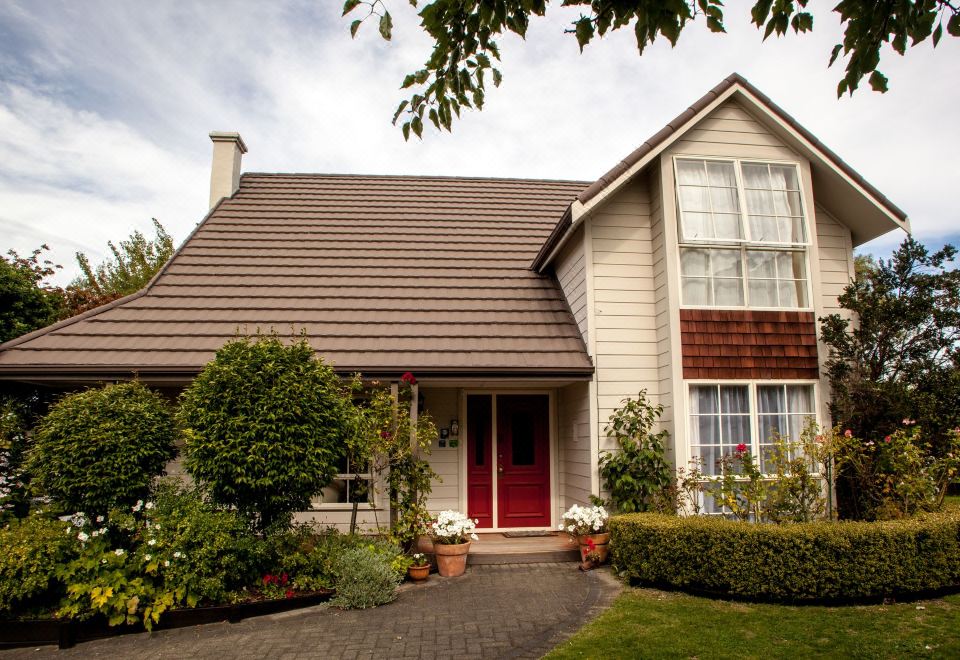 a large , two - story house with a brown roof and white walls , surrounded by greenery and potted plants at The Loft Bed and Breakfast