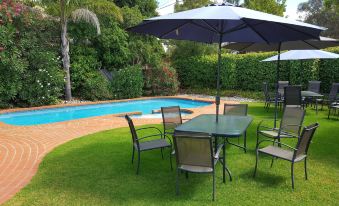 a backyard with a pool , green grass , and an umbrella providing shade , as well as several dining tables and chairs at The Heritage Bendigo