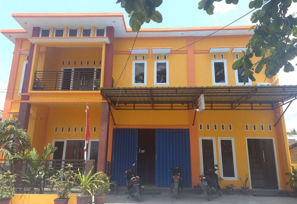 a two - story house with orange walls and blue shutters is surrounded by parked motorcycles on the street at Sinar Harapan
