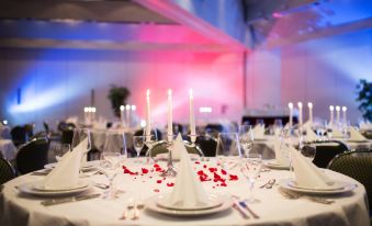 a large banquet hall with multiple tables set up for a formal event , featuring white tablecloths and red rose petals at Achat Hotel Kaiserhof Landshut
