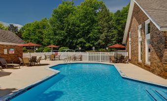 a large swimming pool with a stone wall and patio furniture is surrounded by trees at Residence Inn Hartford Windsor