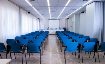 a large conference room with rows of blue chairs arranged in front of a projector screen at Hotel Touring