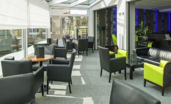 a modern lounge area with black and green chairs , tables , and large windows offering views of the outdoors at Ibis Luxembourg Sud