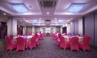 a large conference room with pink chairs and tables , a screen at the front , and hanging lights at favehotel Langko Mataram - Lombok