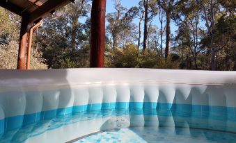 a hot tub filled with water , surrounded by trees and a wooden deck , creating a serene outdoor atmosphere at Jarrah Grove Forest Retreat
