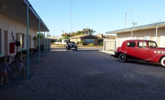 a red car is parked in a parking lot next to a house with a clear blue sky overhead at Kadina Village Motel