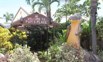 "a tropical garden with palm trees and a sign that reads "" hi welcome to pam 's place .""." at Cooktown Motel