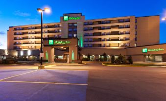 "a large hotel with a green sign that says "" holiday inn "" and has a parking lot in front of it" at Holiday Inn Laval - Montreal