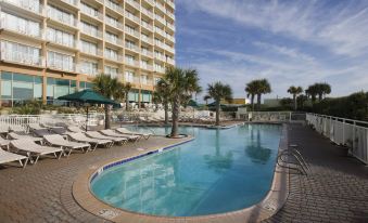 a large outdoor swimming pool surrounded by palm trees , with a hotel building in the background at Courtyard Carolina Beach Oceanfront
