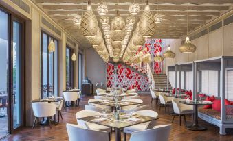 a modern restaurant with white chairs and tables , a red wall , and hanging lights , giving it an elegant and stylish atmosphere at W Goa