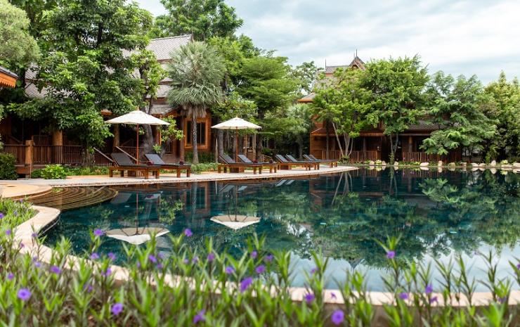 a serene resort with a pool surrounded by wooden buildings , umbrellas , and lounge chairs , reflecting the surrounding natural beauty at Khum Wang Nuea Villa