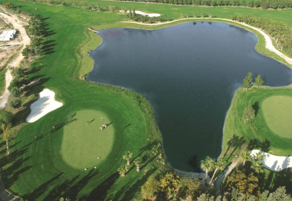 aerial view of a golf course with a lake in the middle , surrounded by green grass at El Plantío Golf Resort