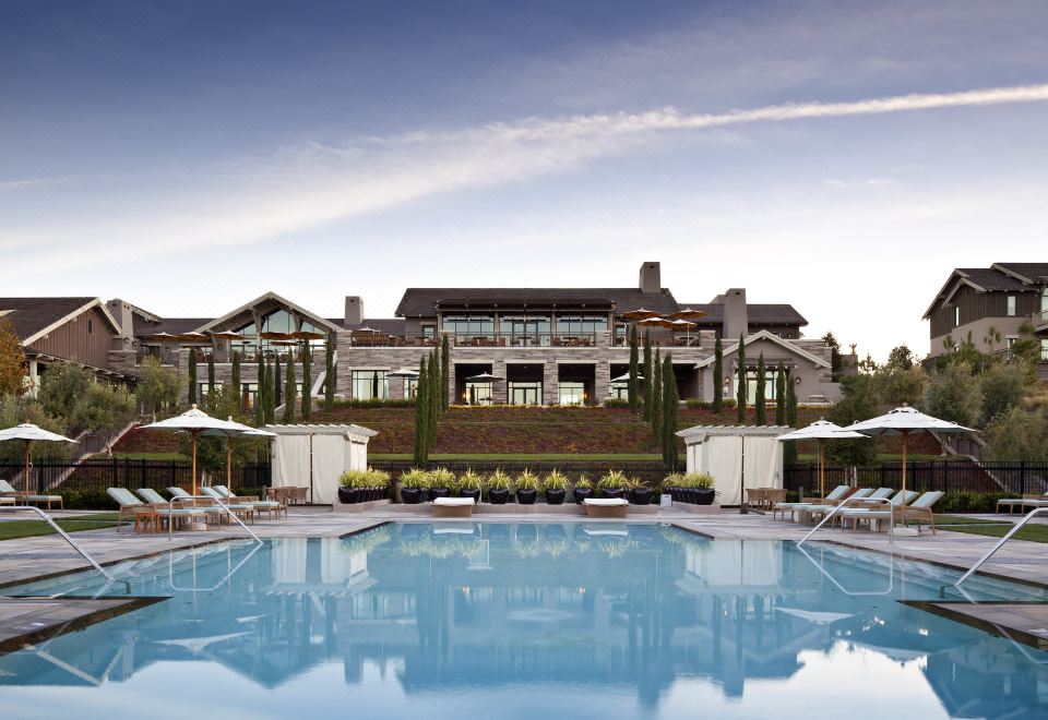 a large swimming pool with lounge chairs and umbrellas in front of a large building at Rosewood Sand Hill