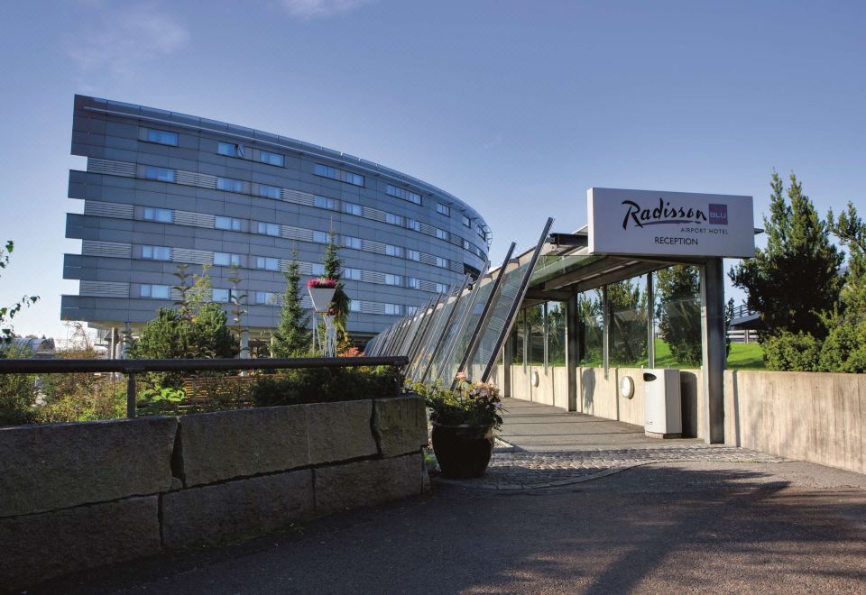 a modern building with a sign for radisson blu hotel , situated on a stone path leading to the entrance at Radisson Blu Airport Hotel, Oslo Gardermoen