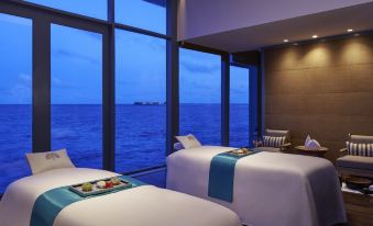 a room with two beds , each bed has a tray of food and drink on it , and a window overlooking the ocean at Raffles Maldives Meradhoo Resort