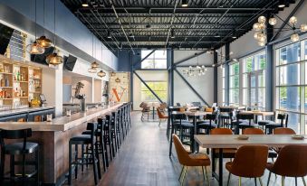 a modern restaurant with wooden floors , metal ceiling , and large windows , featuring a bar area with stools , dining tables , and chairs at Delta Hotels by Marriott Milwaukee Northwest