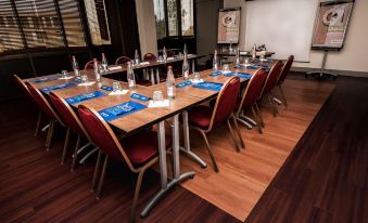 a conference room with a long table set for a meeting , surrounded by chairs and adorned with blue place mats at Campanile Marne la Vallee - Torcy