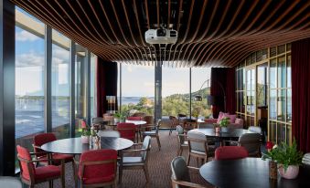 a restaurant with several tables and chairs , a wooden ceiling , and large windows overlooking the ocean at Radisson Blu Caledonien Hotel, Kristiansand