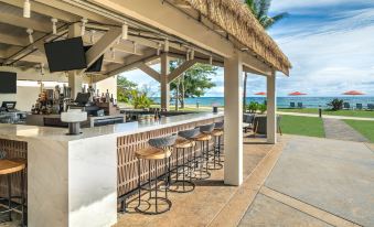 a bar with a thatched roof and stools is shown next to a beach scene at Sheraton Kauai Coconut Beach Resort