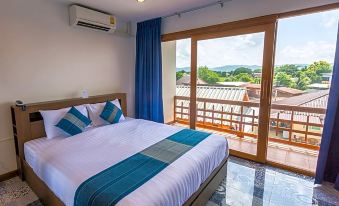 a bedroom with a large bed , blue curtains , and a sliding glass door leading to a balcony overlooking a beautiful landscape at The Indigo House Phrae