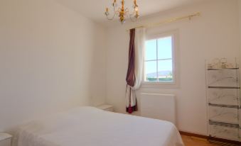 a white bedroom with a large window , a bed , and a chandelier hanging from the ceiling at La Fabrique