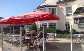 a group of people sitting at outdoor dining tables under a red umbrella , enjoying their meal at Kings Head