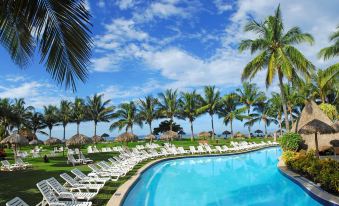 a large swimming pool surrounded by lounge chairs and palm trees , with a blue sky overhead at Fiesta Resort All Inclusive Central Pacific - Costa Rica