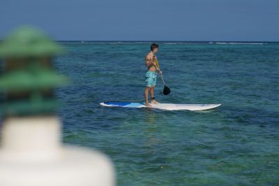 a man is paddleboarding on a blue and white surfboard in the ocean , surrounded by clear blue water at Wyndham Reef Resort Grand Cayman