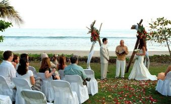 a wedding ceremony taking place on a grassy field near the ocean , with guests seated and officiating at Punta Islita, Autograph Collection
