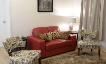 a cozy living room with a red couch , two chairs , and a lamp on the wall at Warrego Hotel Motel Cunnamulla