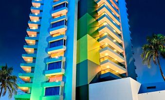 a tall building with a blue and green facade is lit up at night , surrounded by palm trees at Hotel Dann Cartagena