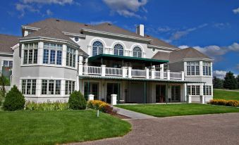 a large , white building with a green roof and balconies is surrounded by a well - maintained lawn and landscaping at Claremont Inn & Winery