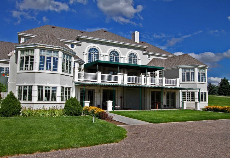 a large , white building with a green roof and balconies is surrounded by a well - maintained lawn and landscaping at Claremont Inn & Winery