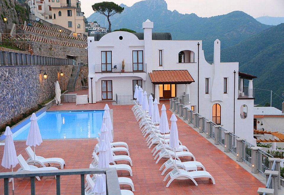 a large white building with a pool and lounge chairs is in the foreground , while mountains are visible in the background at Villa Piedimonte