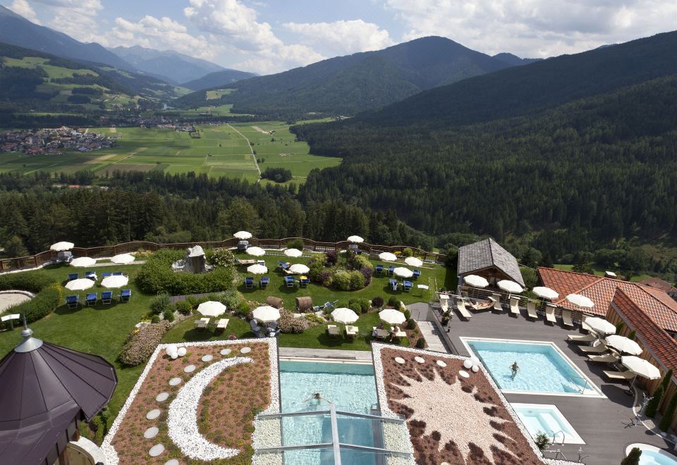 a large hotel with a swimming pool surrounded by mountains , providing a serene and picturesque setting at Alpin Panorama Hotel Hubertus