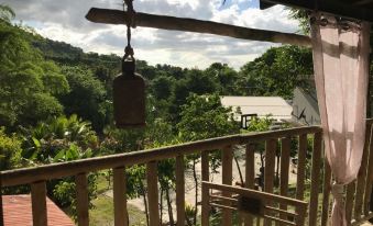 a wooden porch with a hanging light , offering a view of lush greenery and trees in the distance at Hacienda Tres Casitas
