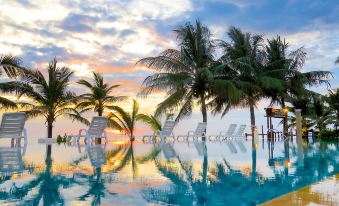 a large outdoor pool surrounded by palm trees , with a beautiful sunset in the background at Chaolao Cabana Resort