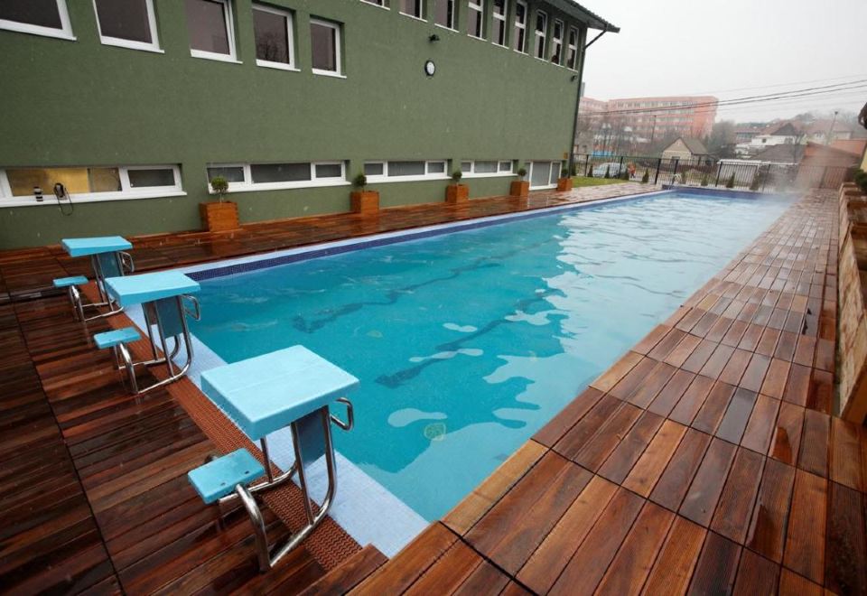 an outdoor swimming pool surrounded by a wooden deck , with several chairs placed around the pool area at Hotel Perla