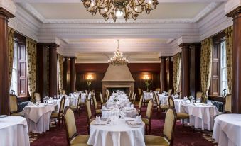 a large dining room with multiple tables covered in white tablecloths and chairs arranged around them at Doxford Hall Hotel and Spa