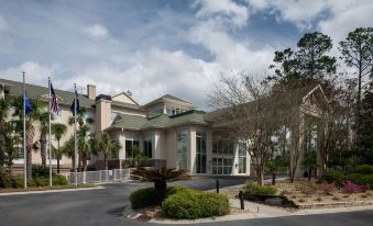 a large building with a green roof , surrounded by trees and bushes , under a blue sky with white clouds at Hilton Garden Inn Hilton Head