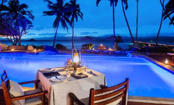 a table with a white tablecloth and wine glasses is set up in front of a pool at night at Jean-Michel Cousteau Resort Fiji