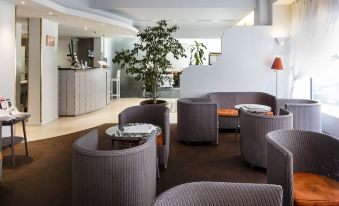 a modern lounge area with gray sofas , wooden floors , and a large tree in the center at Best Western Astoria