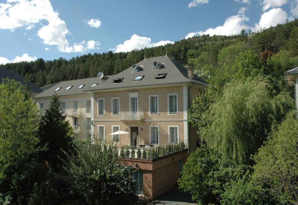 a large house with a balcony on the second floor is surrounded by trees and bushes at Hotel Spa Azteca Barcelonnette