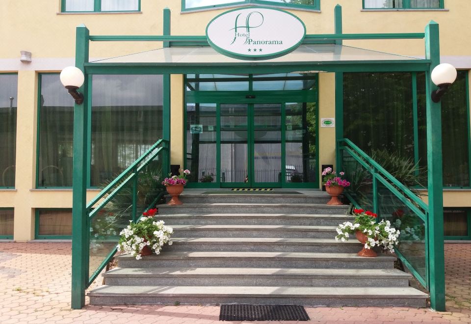 a building with a green and yellow entrance , stairs leading up to the entrance , and potted plants on the steps at Hotel Panorama