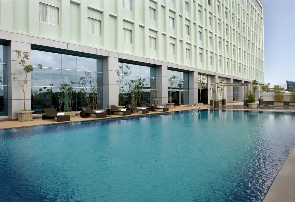 an outdoor swimming pool surrounded by a hotel , with several lounge chairs placed around it at Novotel Bangka - Hotel & Convention Centre